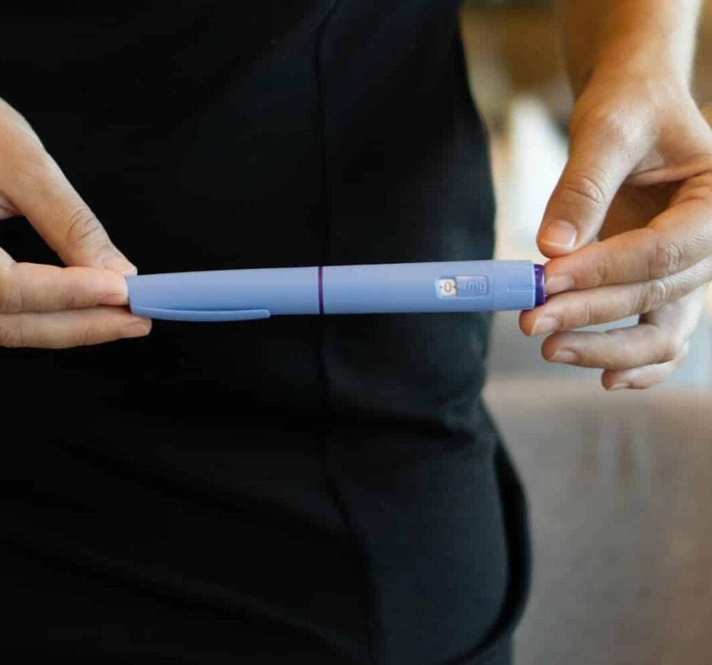 A person holding a blue pen with a purple band, standing against a softly blurred background, emphasizing focus on the pen.
