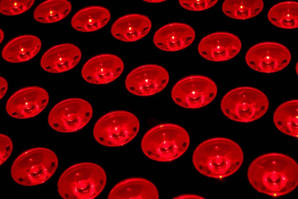 A close-up view of a grid of red circular objects, resembling lenses, illuminated against a dark background.