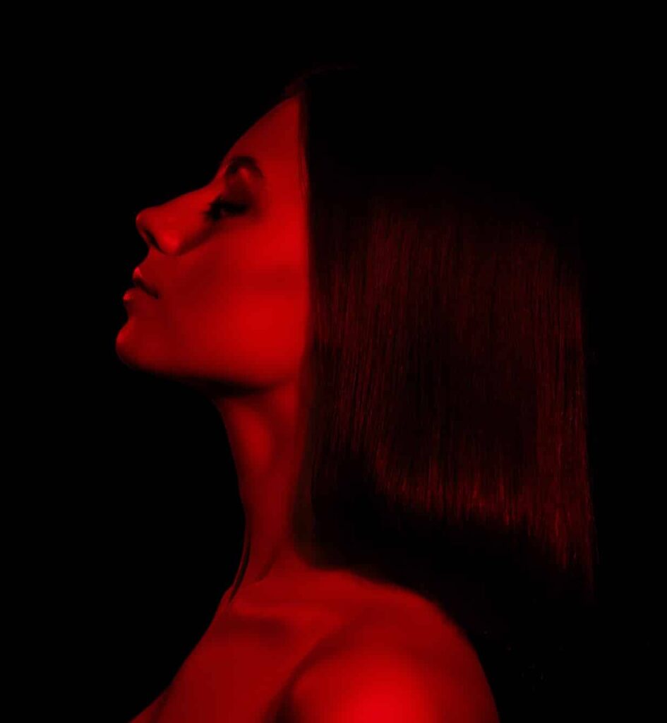 A profile view of a woman with long, straight hair against a black background, illuminated by red lighting, creating a dramatic silhouette effect.